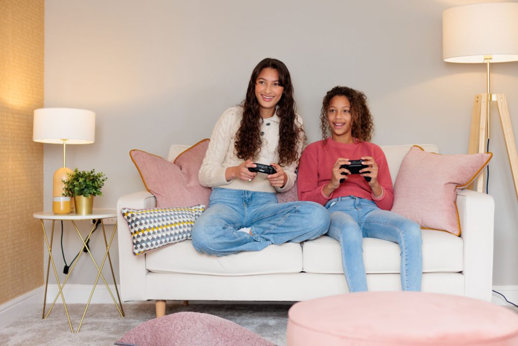 Two girls playing video games on sofa in living room